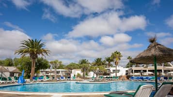 Un área de piscina con sillas de descanso y sombrillas, rodeada de palmeras y edificios.