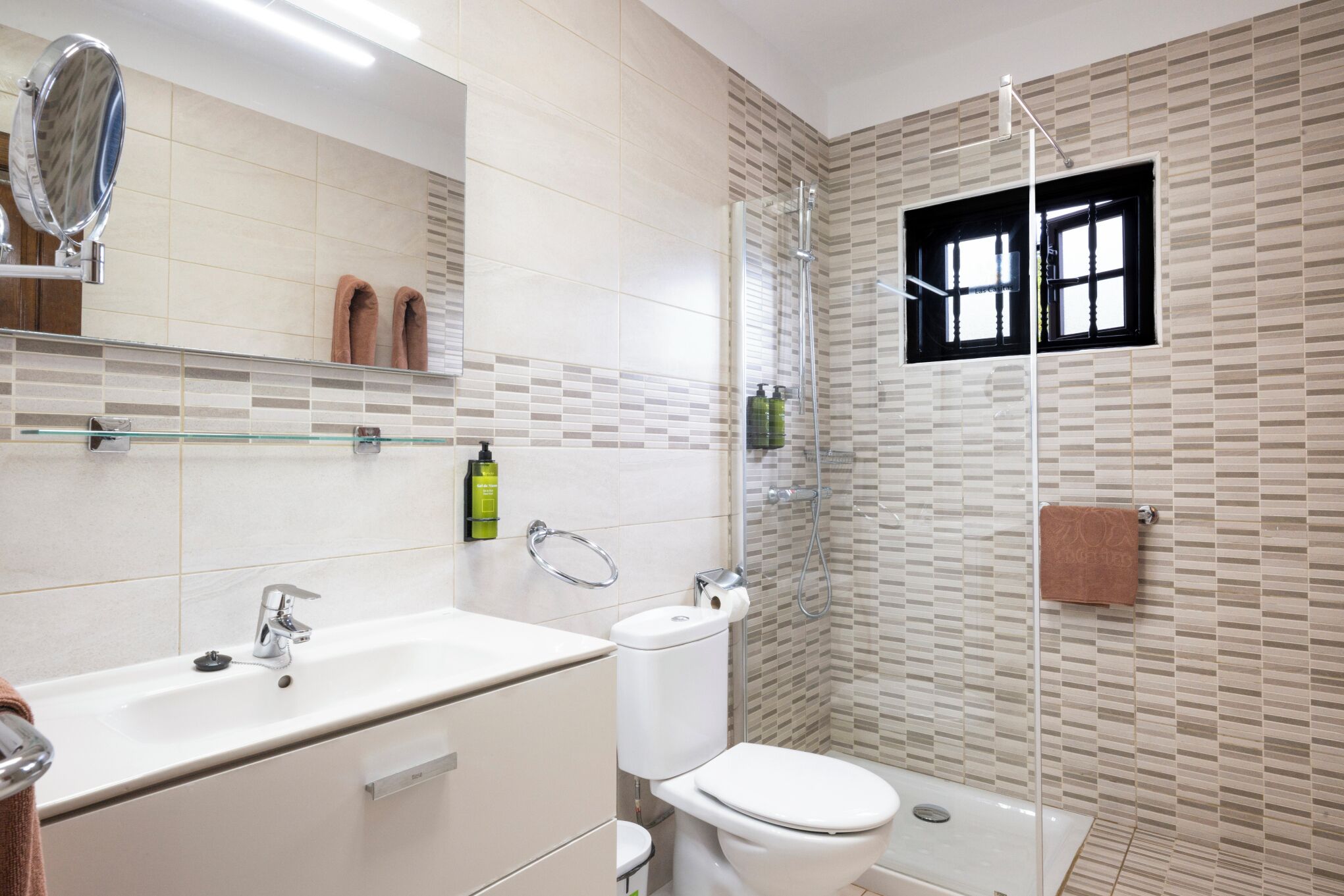 Un baño moderno con lavamanos doble, inodoro y ducha con mampara de vidrio.