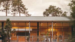 Un bâtiment moderne doté de grandes fenêtres, d’un balcon et entouré d’arbres.