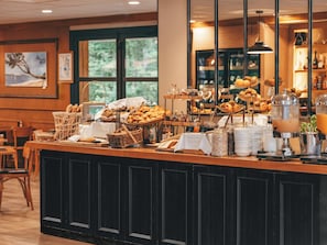 Mostrador de buffet con diversos alimentos, una máquina de café y una zona de estar con sillas.