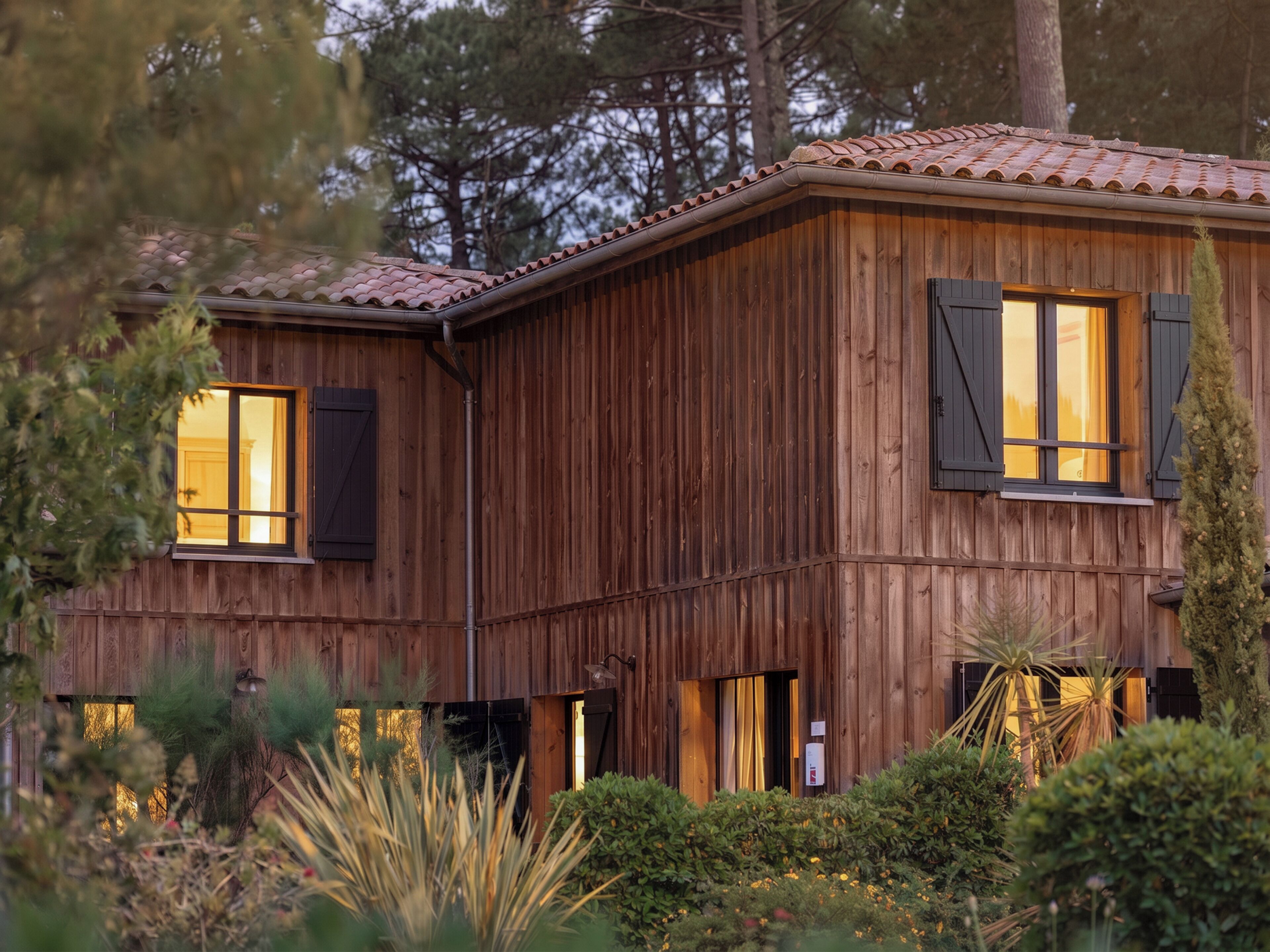 A wooden house with two windows, a door, and a small garden.