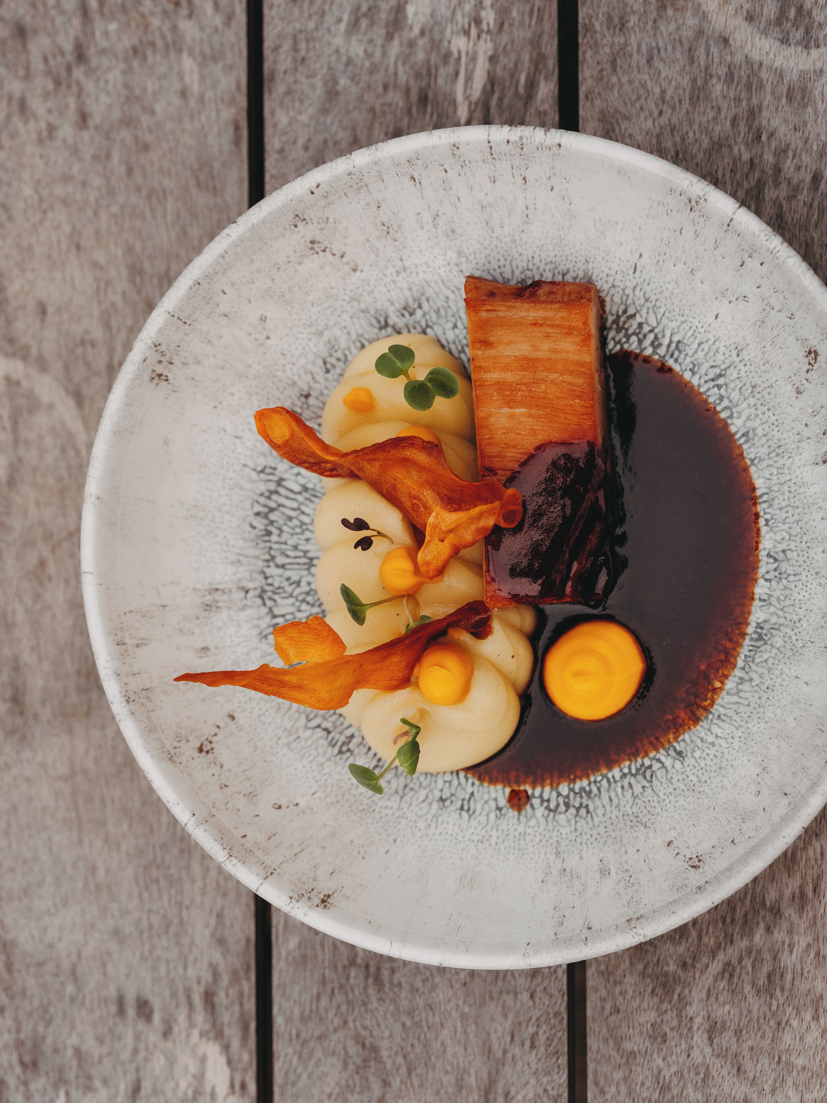 A plate of food with various items including a piece of meat, potatoes, and garnishes.