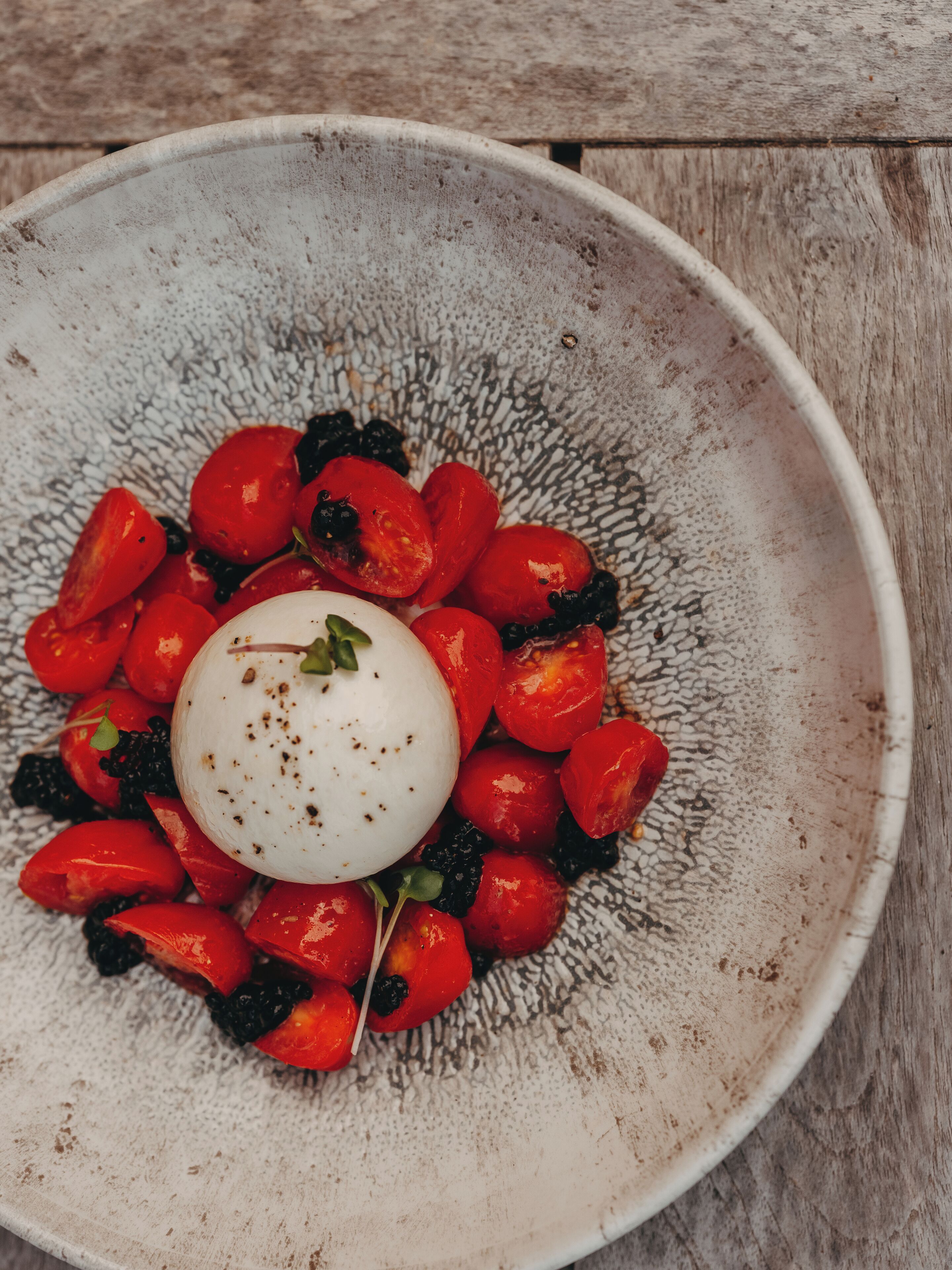A plate with a white spherical food item surrounded by red and black vegetables.
