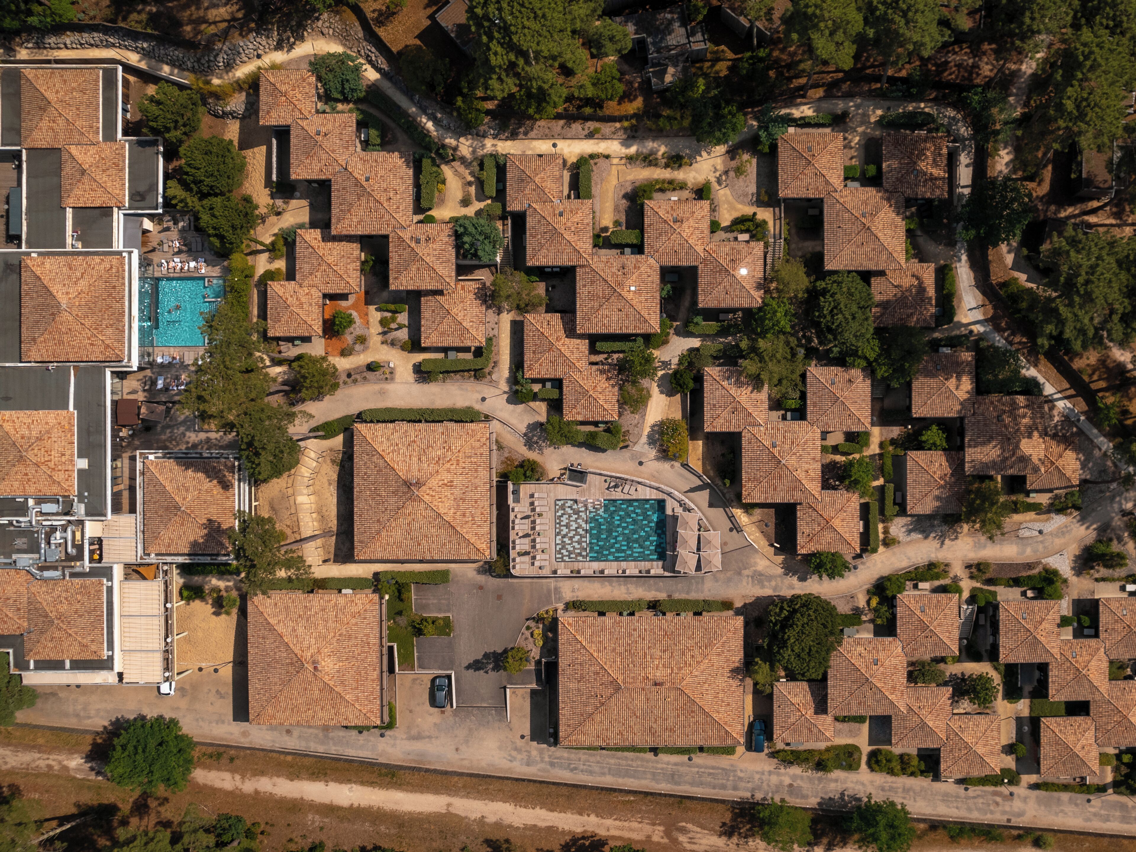 An aerial view of a resort with multiple bungalow-style accommodations, a central swimming pool, and surrounding greenery.