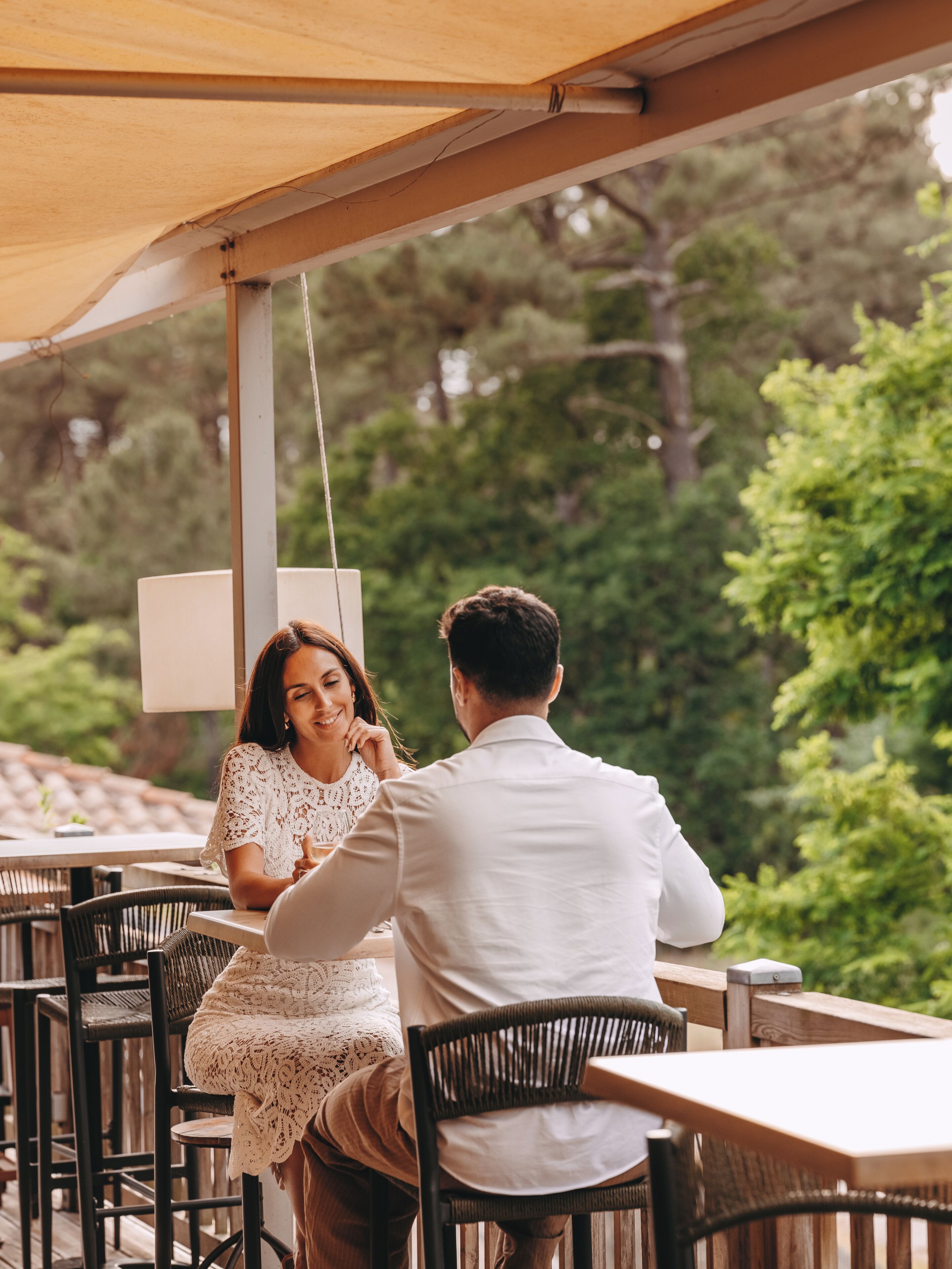 An outdoor seating area with tables and chairs, a canopy overhead, and a view of trees and greenery.