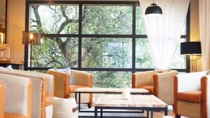 Un coin salon confortable avec des canapés en cuir et une table basse en bois, de grandes fenêtres donnant sur la verdure et un luminaire suspendu.