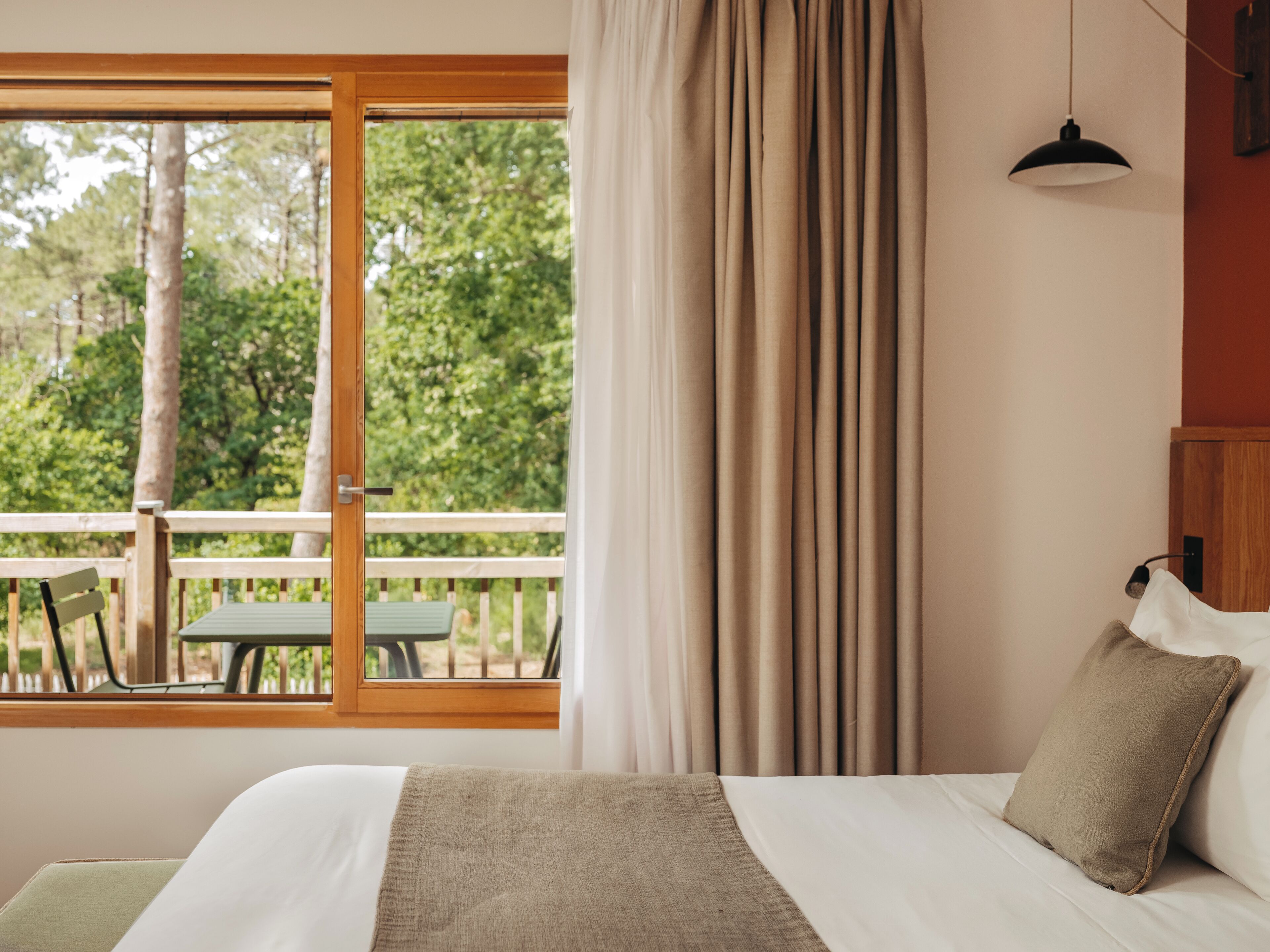 Un dormitorio con un ventanal, vistas a árboles, una terraza de madera exterior y una cama con almohada.