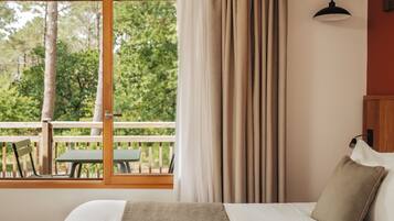 Un dormitorio con un ventanal, vistas a árboles, una terraza de madera exterior y una cama con almohada.