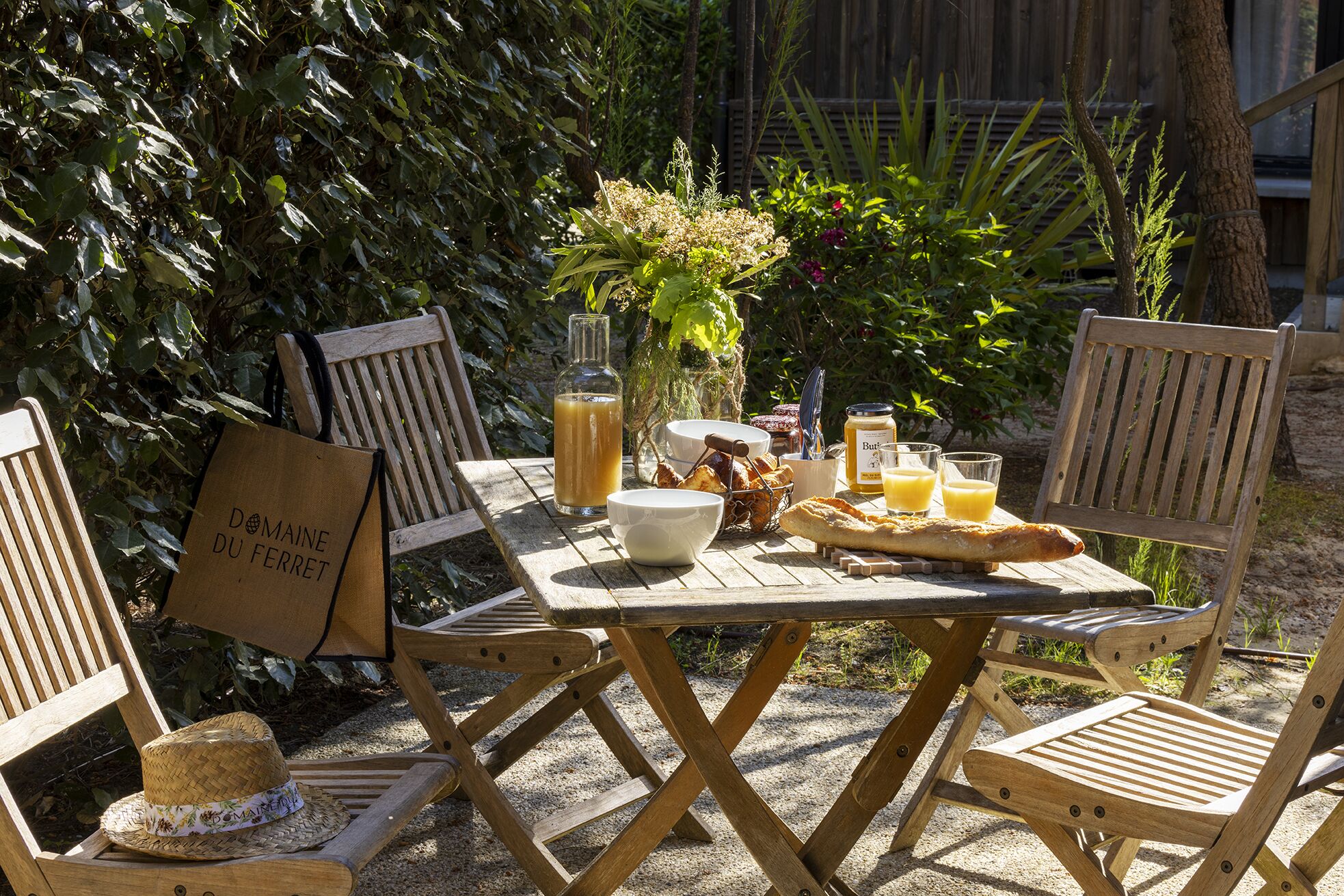 A wooden table with a bottle, bowls, a basket, and a baguette.