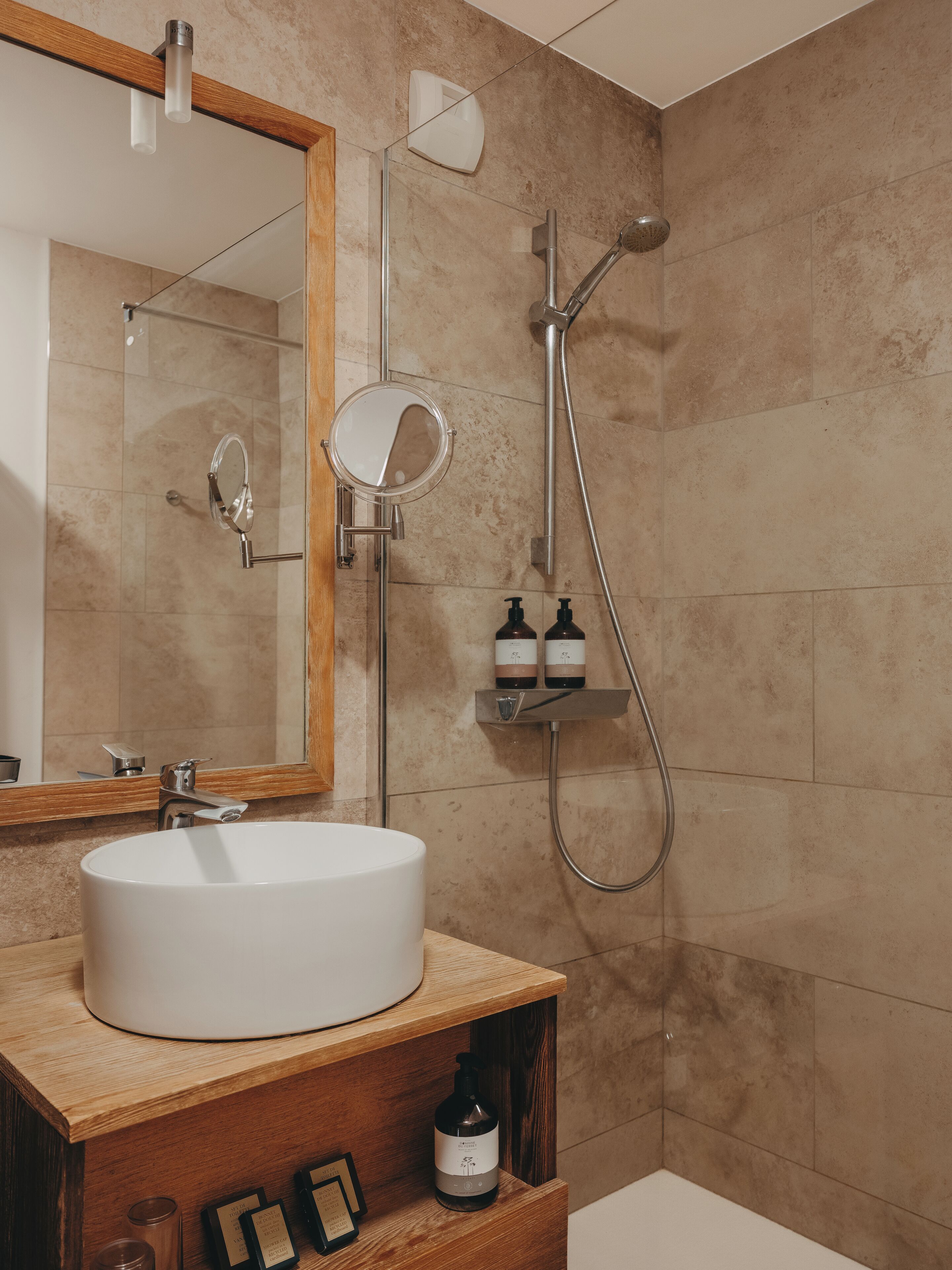 A bathroom with a white sink, a mirror, a handheld showerhead, and a shelf with toiletries.