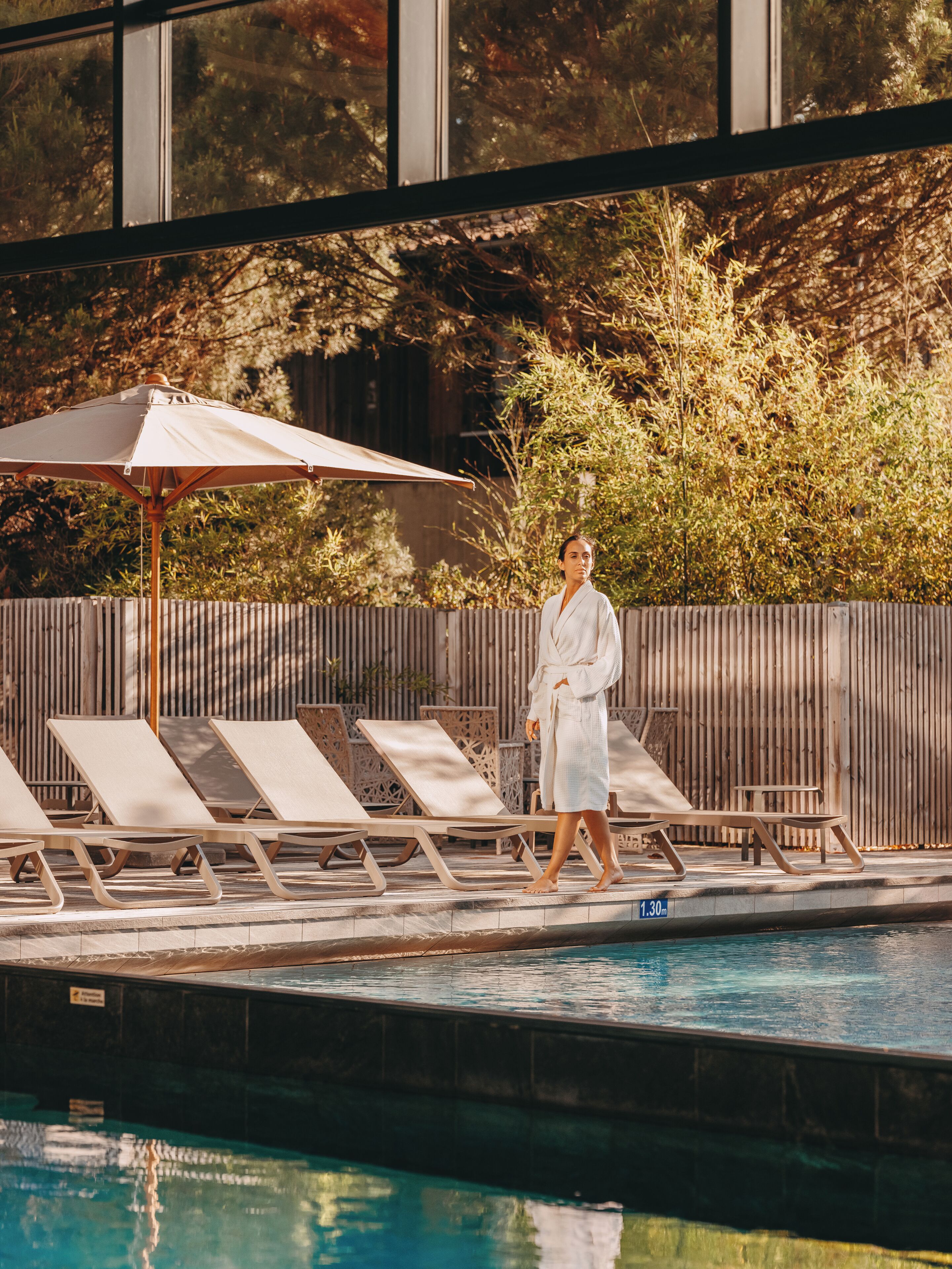 A poolside area with lounge chairs, a wooden fence, and a person in a bathrobe.
