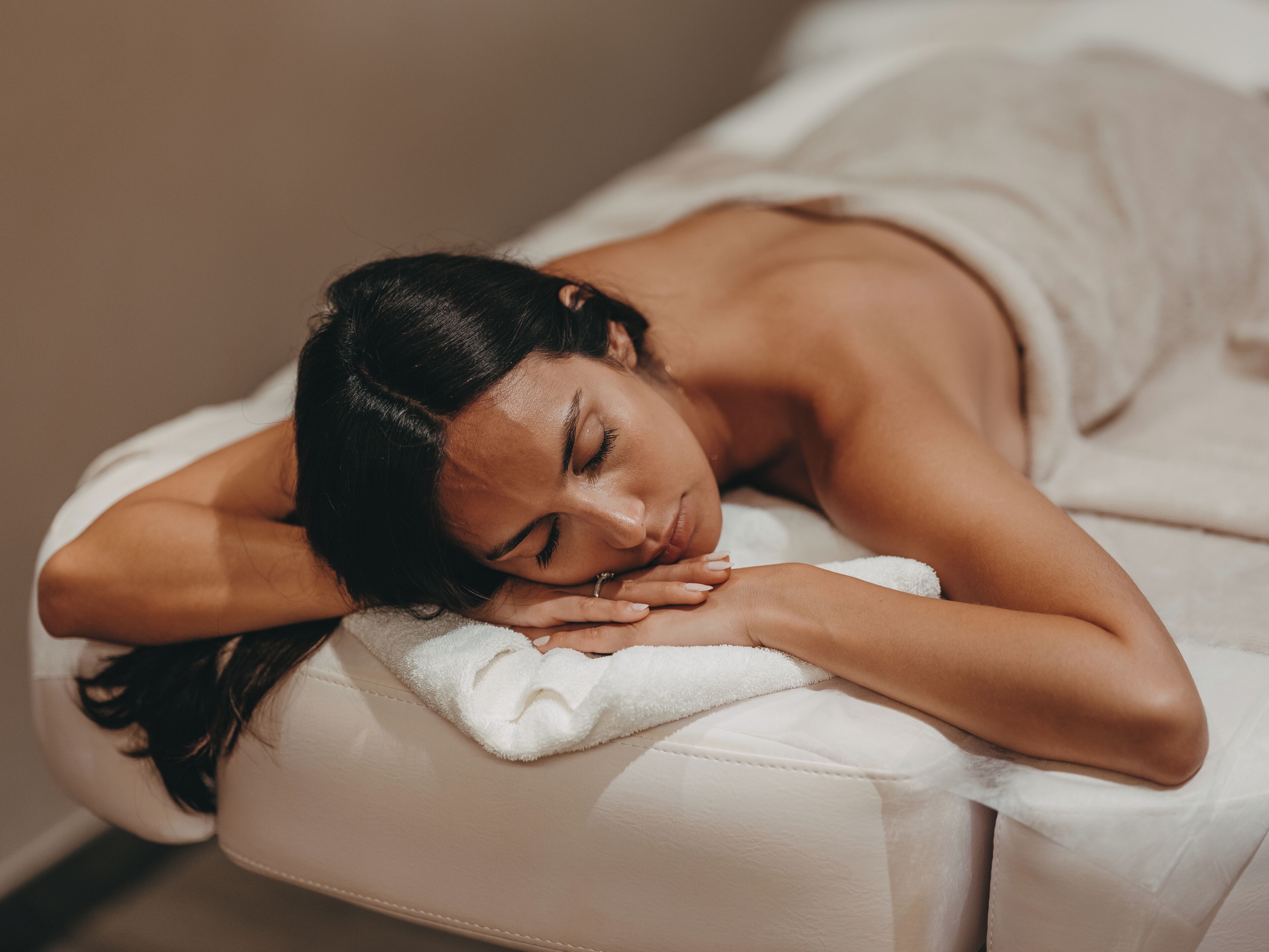 Eine Person liegt auf einer Massageliege in einem Raum mit einer schlichten Wand und einem Fenster.