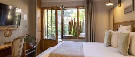Habitación de hotel con una cama grande, un escritorio con silla, televisión y ventana con vistas a árboles.