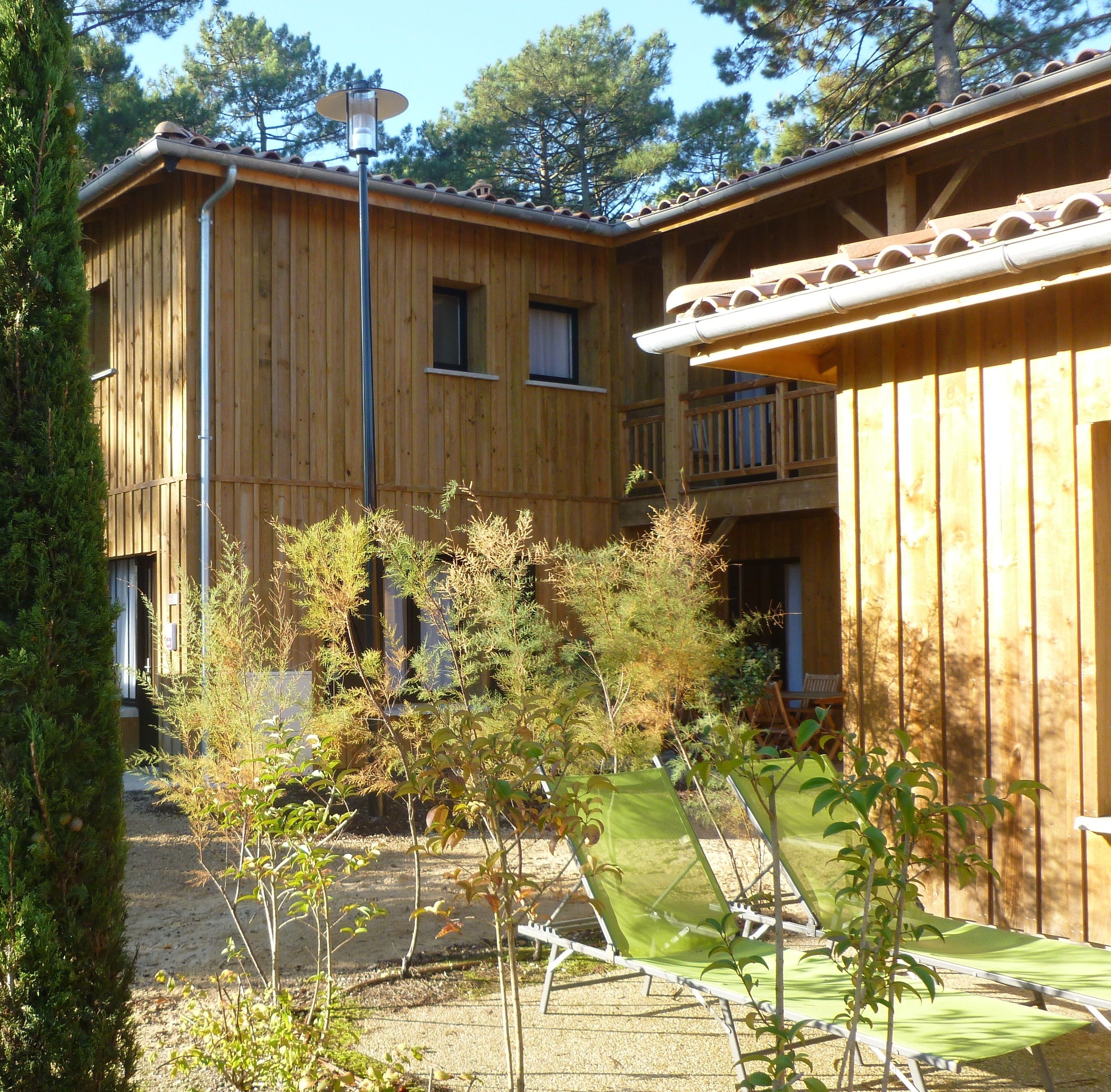 A wooden building with a balcony, a gravel path, and green plants.