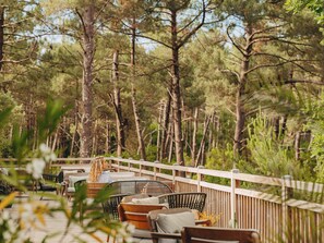 Een terras met houten meubels en een houten balustrade, omgeven door bomen.