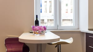 A dining area with a table, a chair, a wine bottle, and a vase with flowers. - Apartments Raic (Dubrovnik)