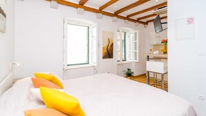 A bedroom with a bed, a desk, and a chair. There are windows and a painting on the wall. - Apartments Raic (Dubrovnik)