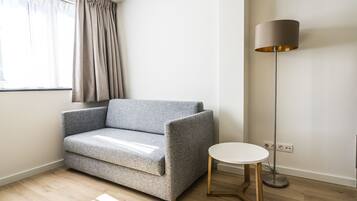 Een moderne woonkamer met een grijze bank, een klein rond tafeltje en een vloerlamp.