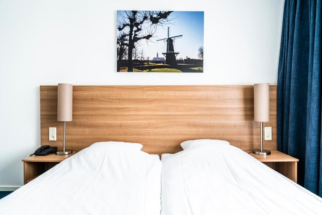 Ein Hotelzimmer mit einem hölzernen Kopfende, zwei Nachttischen mit Lampen, einem Telefon und einem Bett mit weißer Bettwäsche.