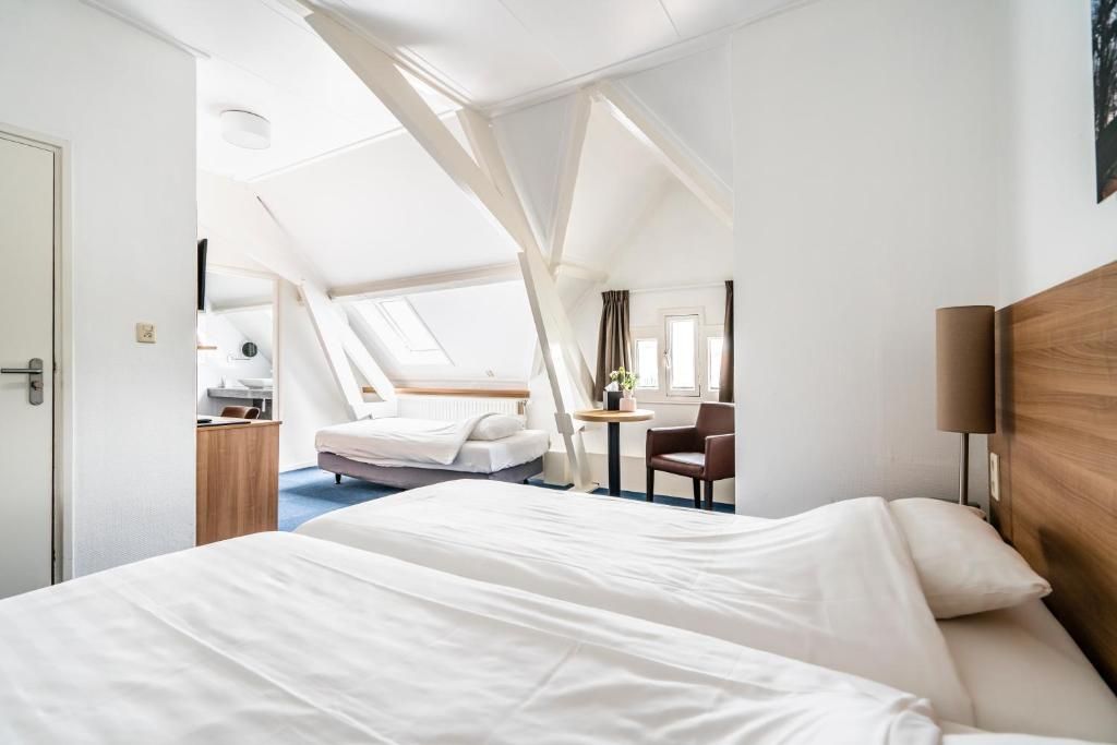 Een hotelkamer met een groot bed, een klein bed, een bureau, een stoel en een raam met gordijnen.