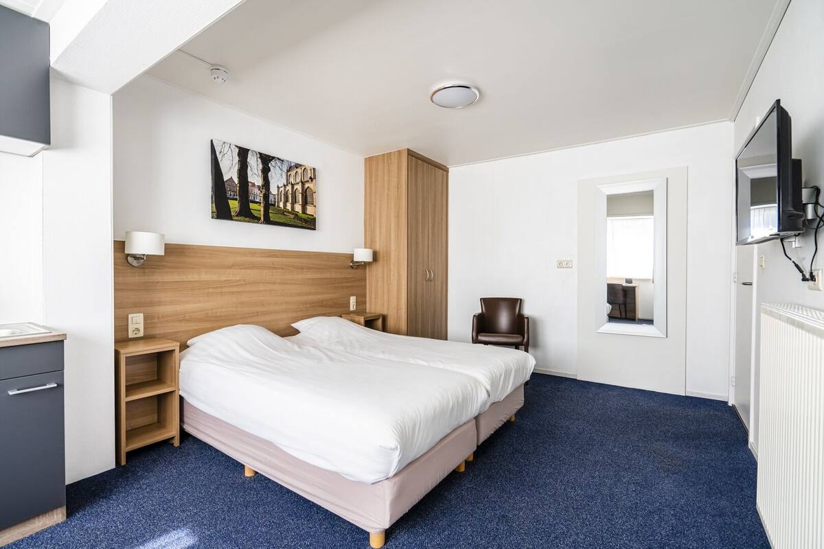 Et moderne hotelværelse med en stor seng, et træhovedgærde, et skrivebord med stol, et fjernsyn og et billede på væggen.