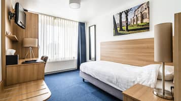 Una habitación de hotel con cama, escritorio, silla, lámpara y un cuadro en la pared.