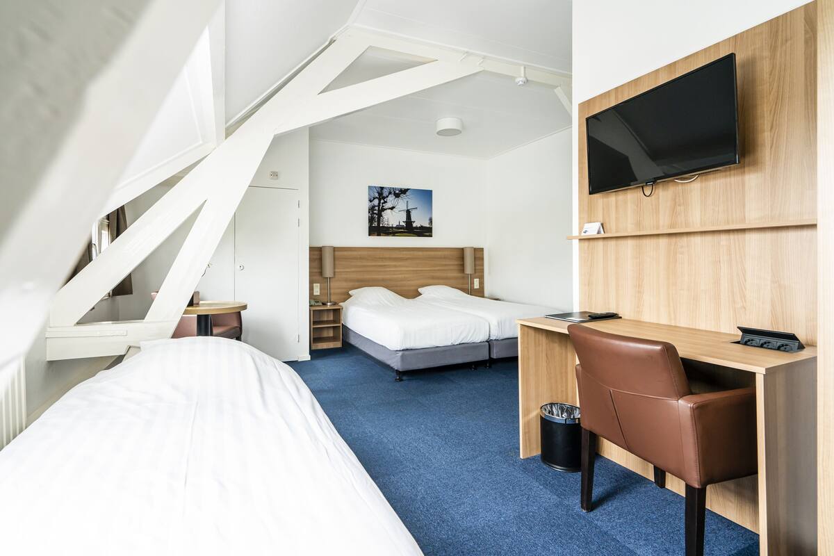 Et hotelværelse med seng, skrivebord, stol, fjernsyn og et billede på væggen.