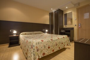 A hotel room with a bed, bedside lamps, a wardrobe, a desk, and a mirror.