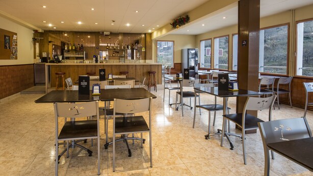 A spacious restaurant with a bar area, multiple tables and chairs, and large windows offering a view of the outdoors. - La Mola (Encamp)