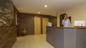 A reception desk with a person standing behind it, a wooden door, and a wall-mounted sculpture. - La Mola (Encamp)