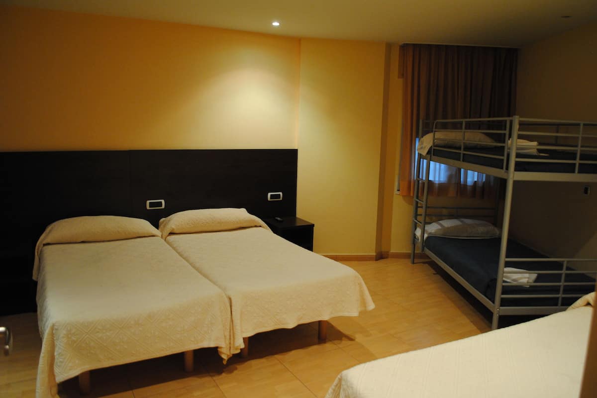 A hotel room with two single beds, a bunk bed, a nightstand, and a wall-mounted TV.