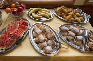 A buffet table with various food items including watermelon slices, bananas, apples, and pastries.