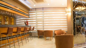 Una hall d'albergo con reception, area salotto e un bar con bicchieri esposti.