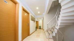 Un corridoio d'albergo con pavimento in marmo, porte in legno e una scala con ringhiere in metallo.