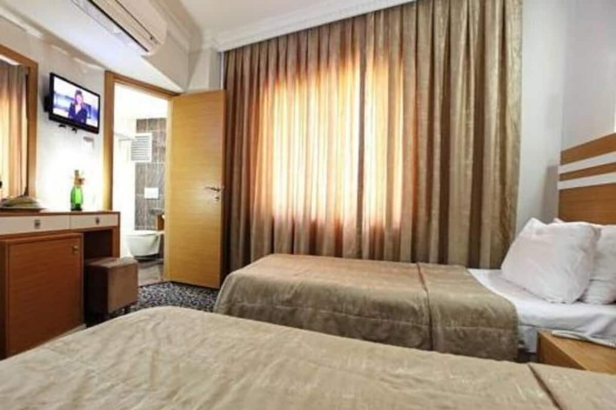 Une chambre d’hôtel avec deux lits, une télévision, un bureau en bois et une salle de bain visible à travers une porte ouverte.