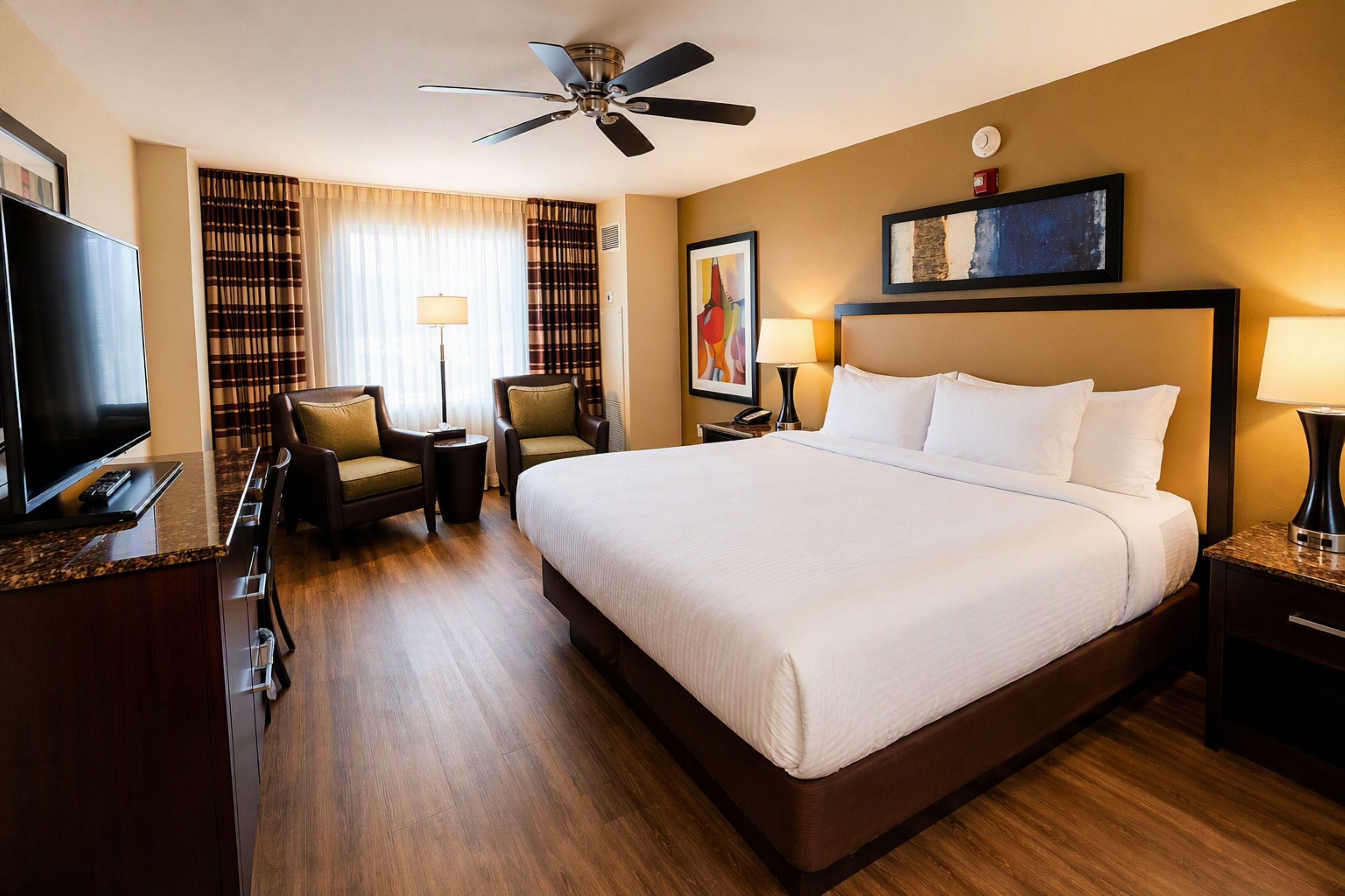 A hotel room with a large bed, a television, a desk, and a ceiling fan.
