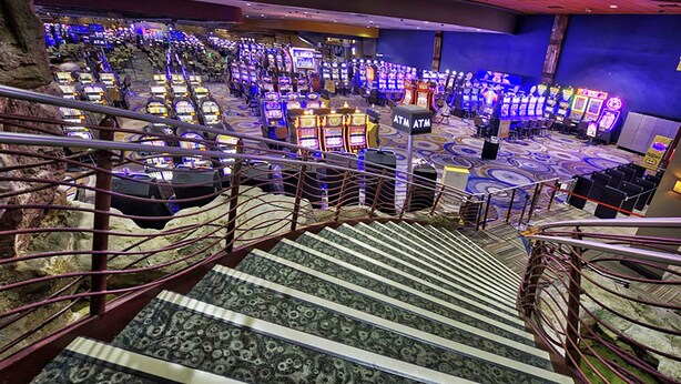 A casino with multiple gaming machines, an ATM, and a staircase leading to upper levels. - Isle of Capri Casino Hotel Boonville & Casino - A Caesars Rewards Destination (Boonville)