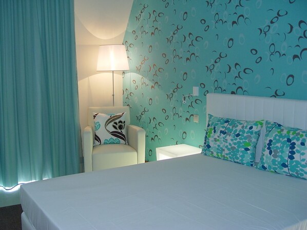 A hotel room with a bed, a chair, a nightstand, and a wall with a pattern. - Apartamentos Atlântida Lido (Funchal)