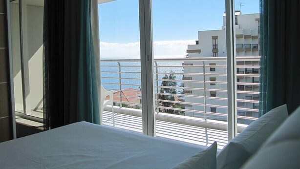 Habitación de hotel con balcón que da al mar y edificios.