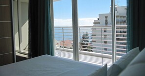 A hotel room with a balcony overlooking the sea and buildings. - Apartamentos Atlântida Lido (Funchal)