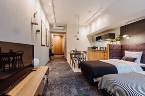 A modern hotel room with a bed, bedside table, and a small desk with a chair. There is a kitchen area with cabinets and a microwave. - Mosquito Silesia Apartments (Katowice)