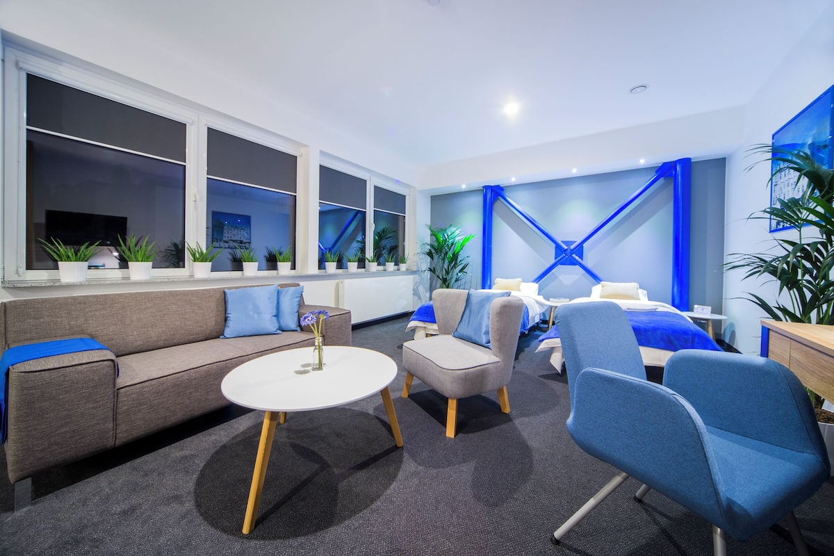 A modern office space with a sofa, chairs, a round table, and a bed.
