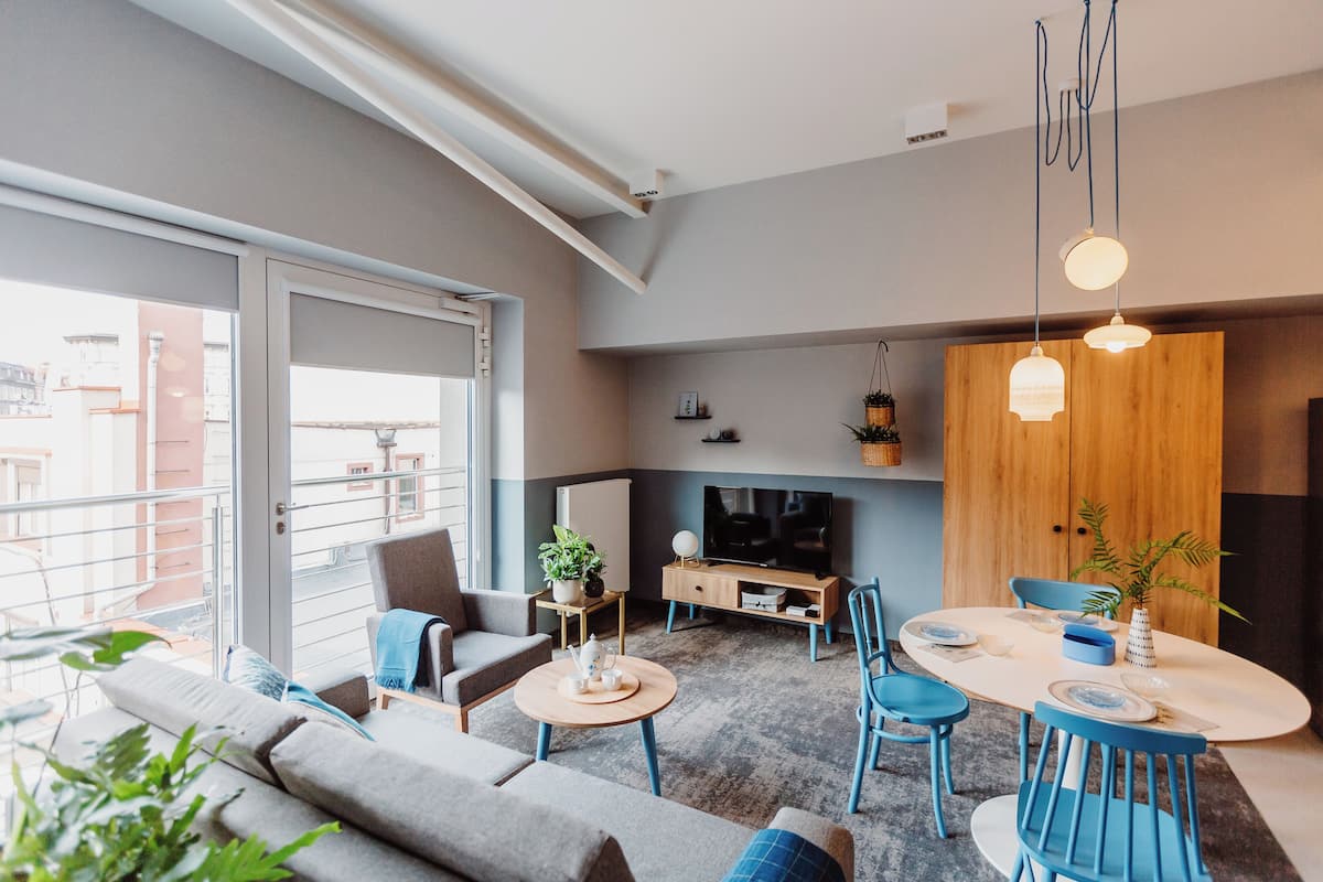 A modern living room with a sofa, chairs, a coffee table, a TV, and a dining area with a table and chairs.