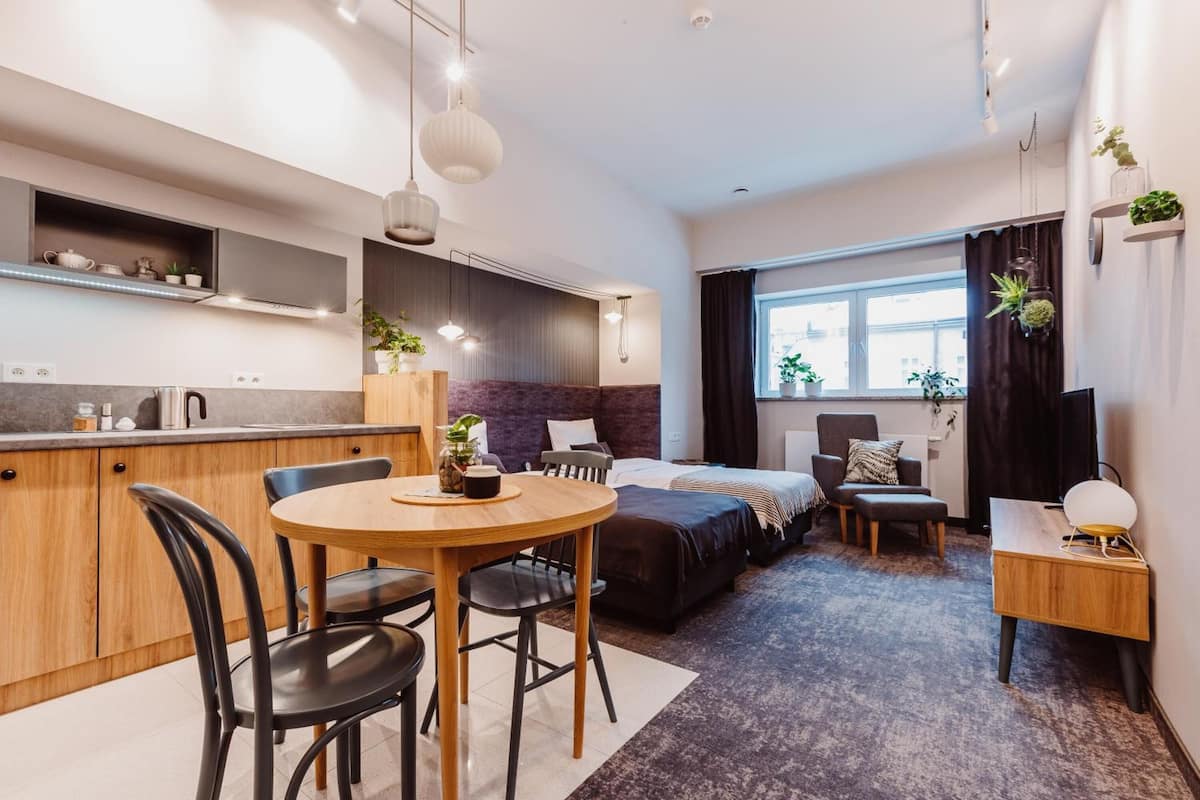 A compact hotel room with a kitchenette, a dining area, a bed, and a small seating area.