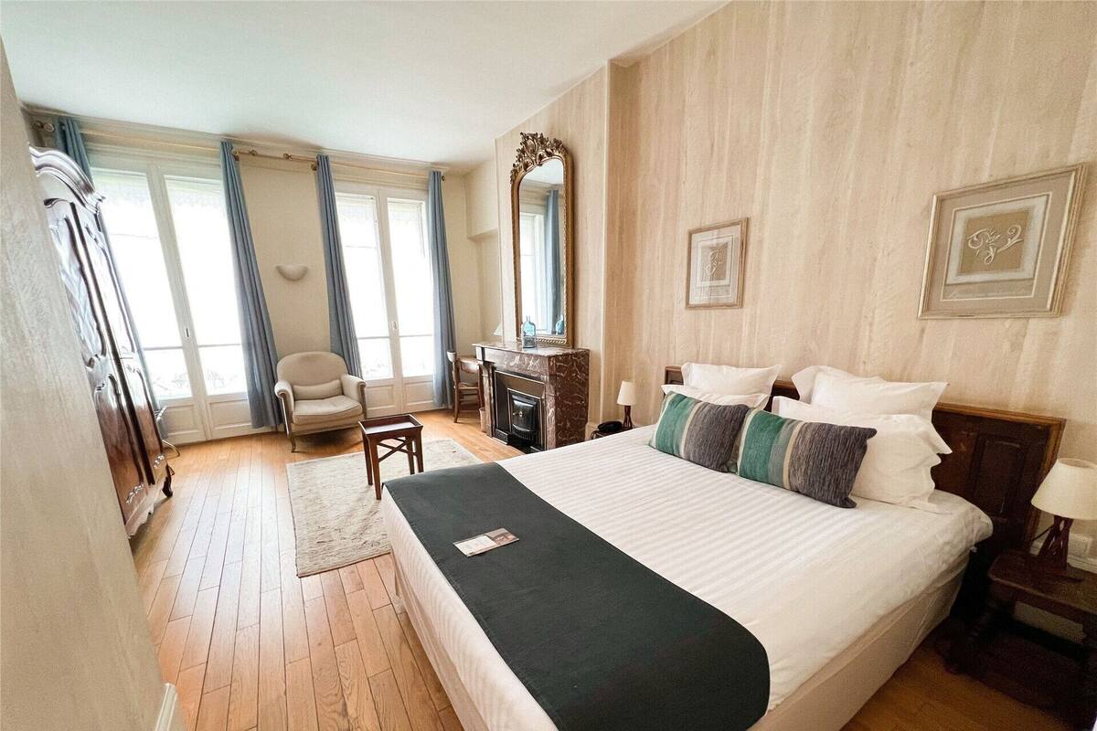 A hotel room with a large bed, a desk, a chair, a fireplace, and a large mirror.