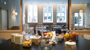 Un comedor de hotel con mesas preparadas para el desayuno, ventanas amplias y vista a la ciudad.