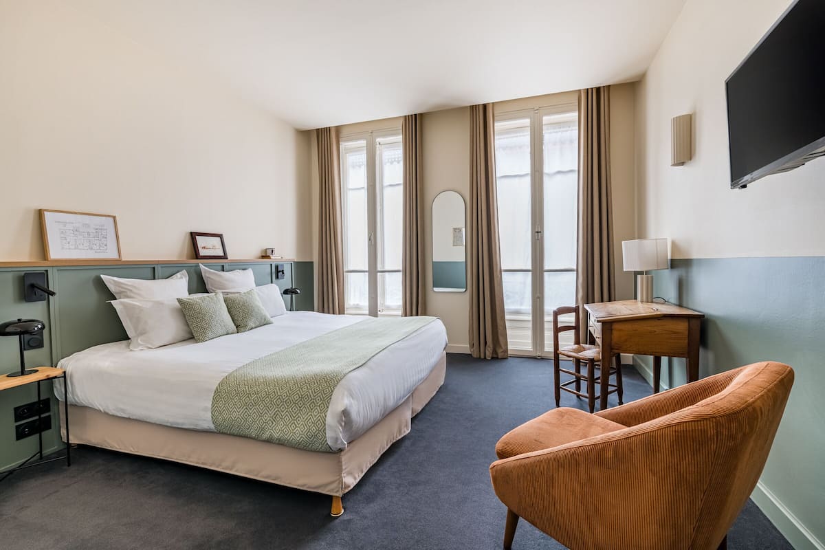 A hotel room with a large bed, a desk, a chair, a TV, and a window with curtains.