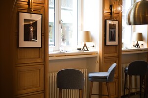Um quarto com painéis de madeira, dois bancos altos, uma janela com vista e quadros nas paredes.