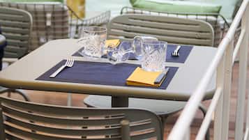 A dining area with metal chairs and tables, each set with cutlery and a glass.
