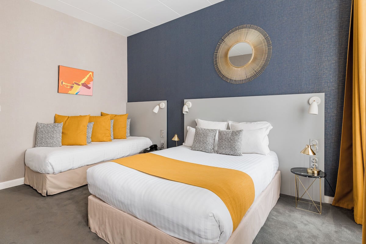 A hotel room with two beds, a large mirror, a small table with a lamp, and a decorative wall piece.
